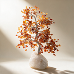 Carnelian crystal tree on an ivory background, glowing amber and orange stone chips on a clear quartz cluster base