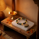 Crystal bracelet and pyrite coin cleansing overnight on the Selenite Zibu plate beside a lit diya
