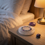The Calm Ritual on a bedside table at night - selenite plate, bracelet, amethyst palm stone and lepidolite tumble